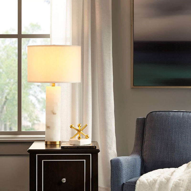 an illuminated white ceramic table lamp placed on a nightstand