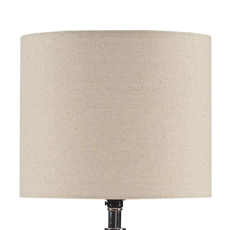 the drum-shaped shade of a white ceramic table lamp