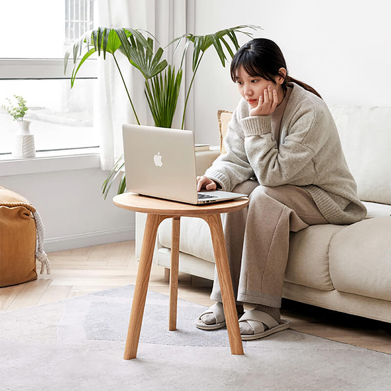 a laptop placed on a round wood end table, with a woman working on the laptiop