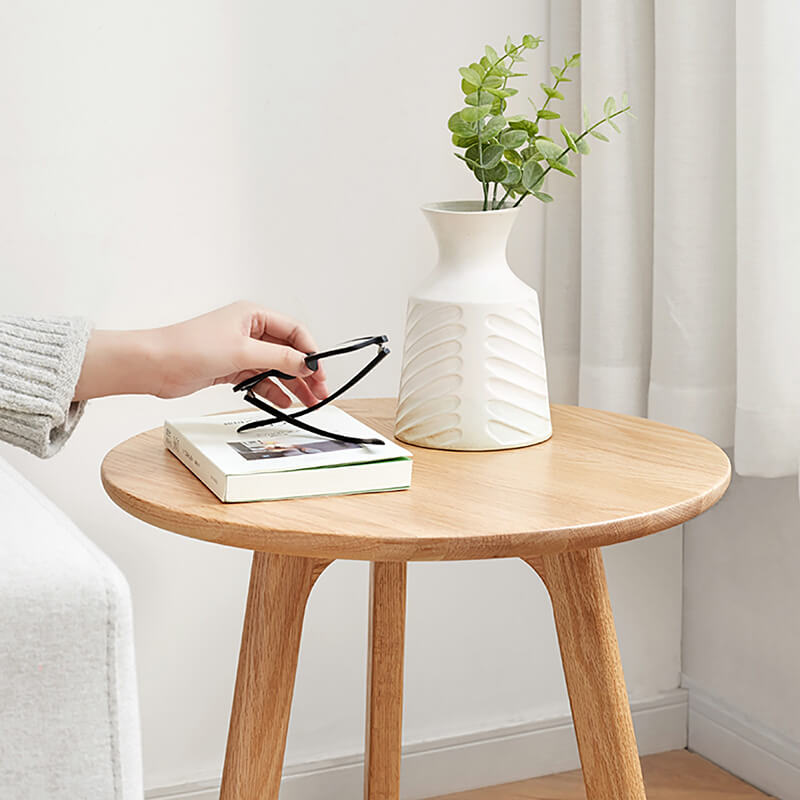 a round wooden end table with a flower vase and a book placed atop