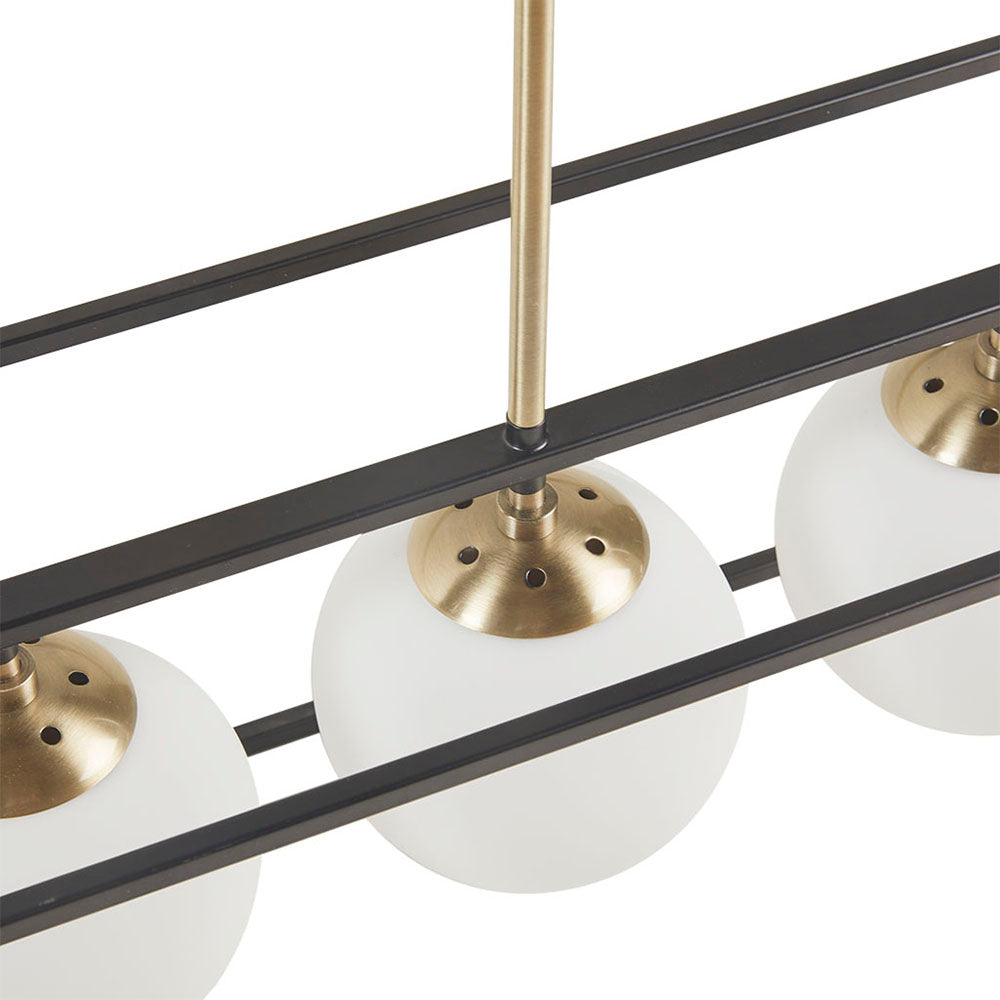 Close view of linear dining chandelier highlighting open brass cage and frosted glass globe