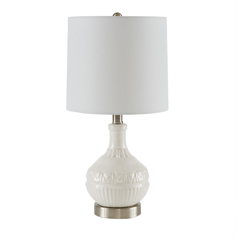 Full view of the white ceramic table lamp with white lamp shade and patterned ceramic base turned on