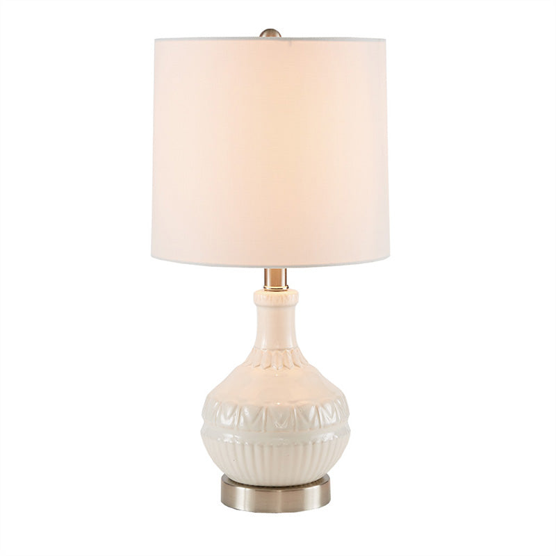 Full view of the white ceramic table lamp with white lamp shade and patterned ceramic base turned on