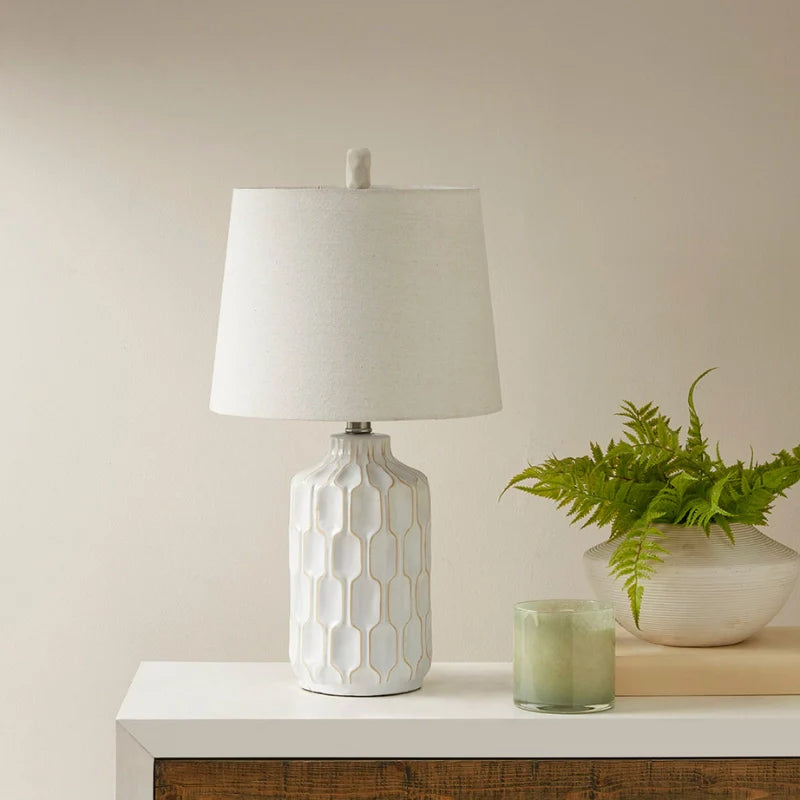 Ivory and white ceramic table lamp with contoured base on a side board 