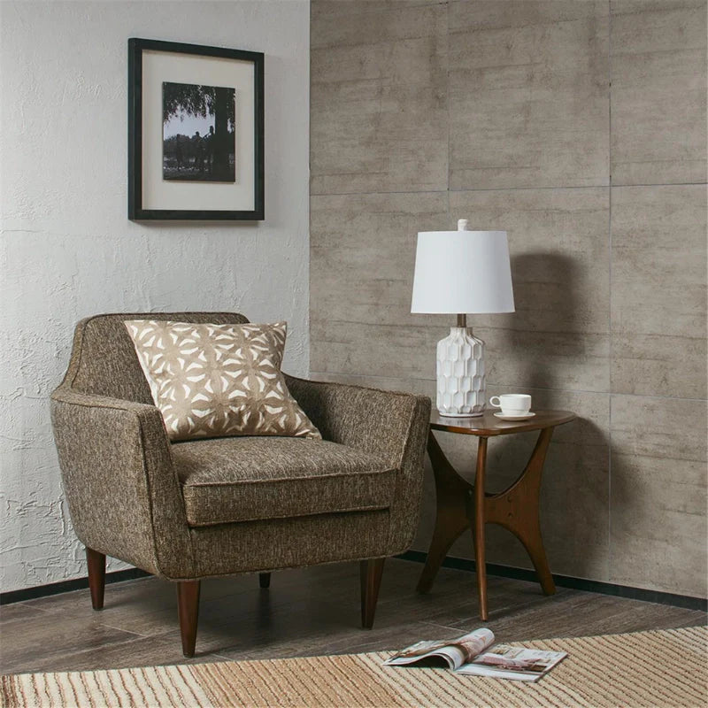 A turned off Ivory and white ceramic table lamp with contoured base on a side table beside a lounge armchair