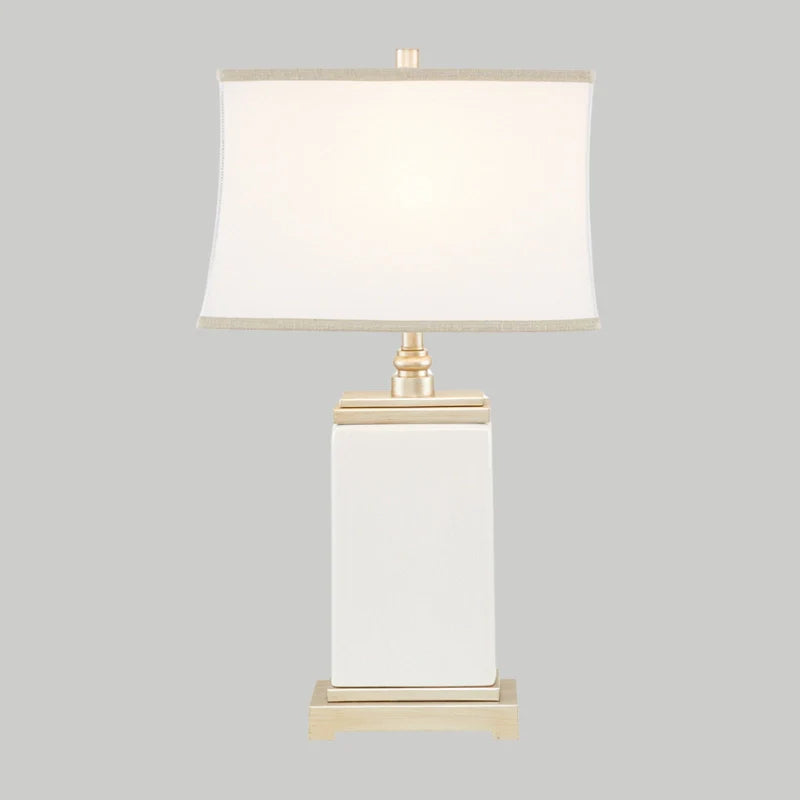 Full view of Ivory Ceramic table lamp turned on with rectangular base and lampshade