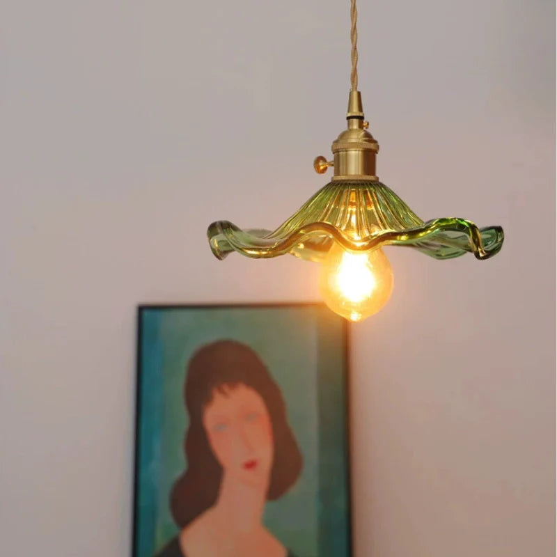 Ceiling mounted green glass pendant light showing illuminated bulb, floral glass lamp shade and brass lamp holder