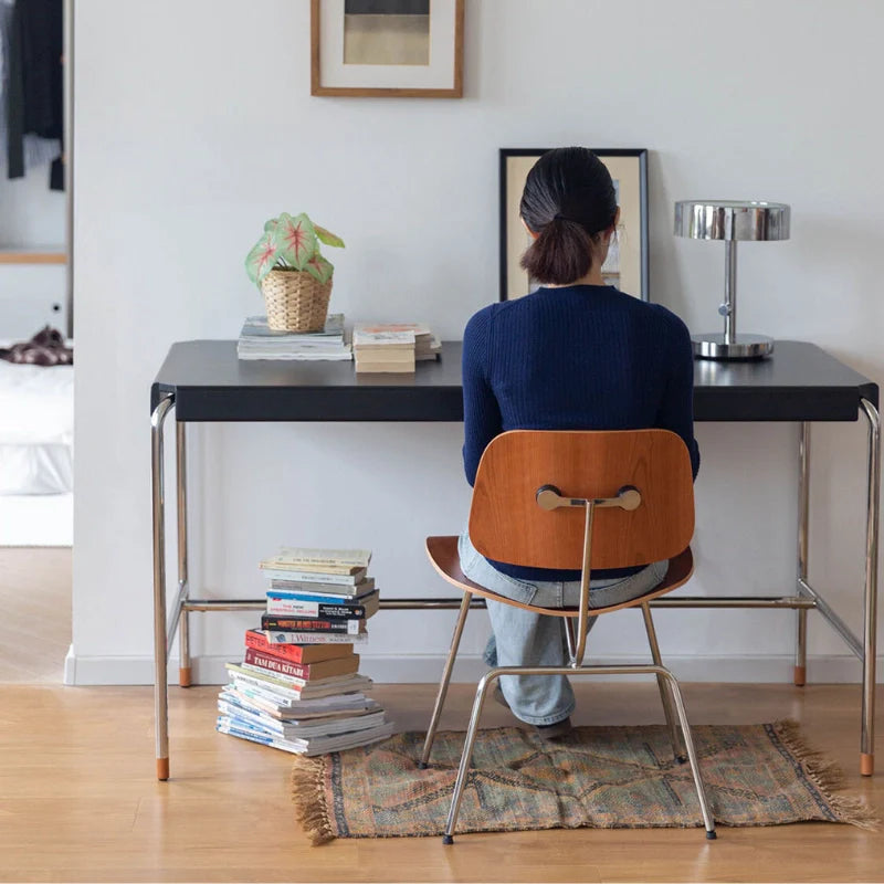 a mid-century modern desk with stainless steel legs and a black wooden tabletop