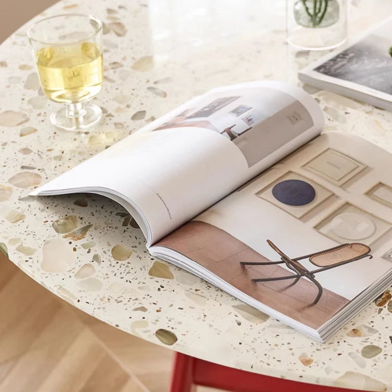 a solid wood dining room table with sintered stone top, an opened magazine, and a glass of wine