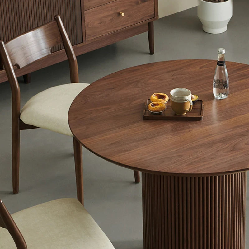 An Up-close image of the Wooden Pedestal Dining Table in rich walnut color, showcasing the fine groovy design on its pedestal and its smooth table top for serving