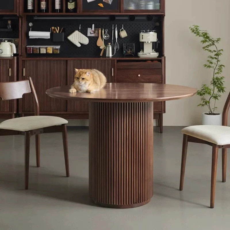 A Round Wood Pedestal Dining Table occupying a dining space in Rich Walnut Color, with Two Cushioned Dining Chairs