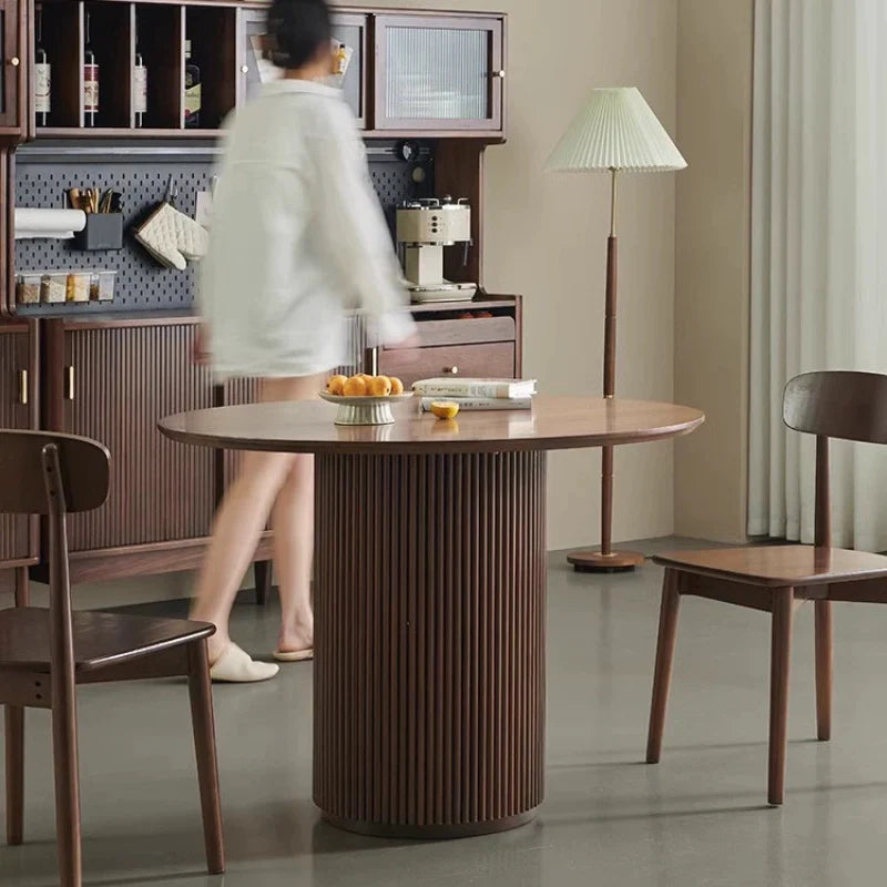 Image of the Round Pedestal Dining Table in a Modern Dining Area in Rich Walnut Color, Providing a Stable Surface for Serving and Placing Books.