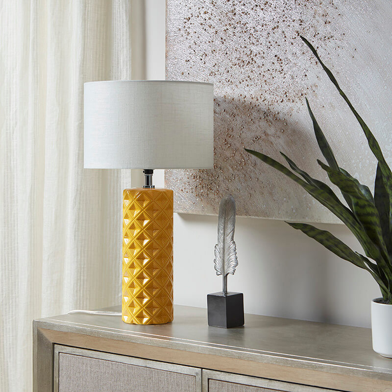 a yellow geometric ceramic table lamp placed on a console table